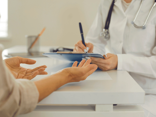 Doctor writes notes on clipboard while patient explains symptoms during a healthcare appointment