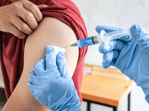 Healthcare worker administers vaccine shot into patient’s arm using syringe and cotton swab preparation