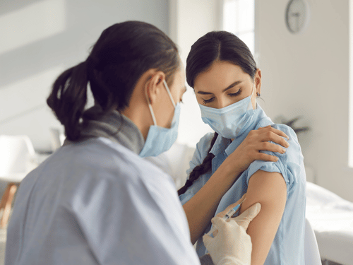 Nurse gives young woman a vaccine injection at Clementi Clinic, both wearing protective face masks