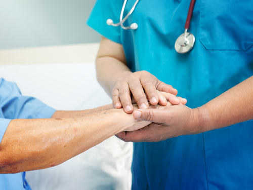 Nurse gently holds elderly patient’s hands during a comforting full body checkup in clinic