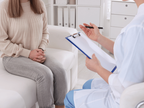 A woman speaks with a healthcare provider holding a clipboard during a medical consultation session