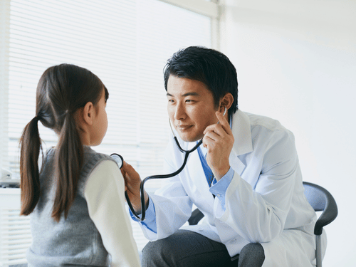 A male doctor uses a stethoscope to listen to a young girl's heartbeat in clinic