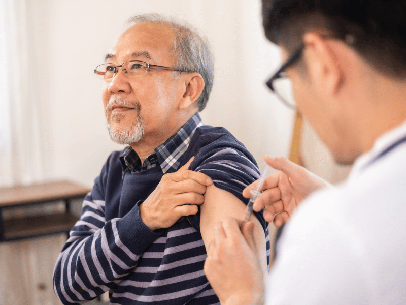 Elderly man rolls up his sleeve to receive a vaccine shot from a healthcare professional