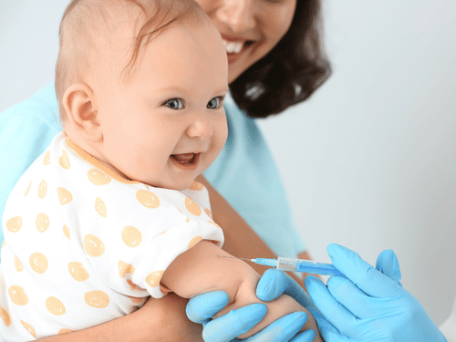 Baby smiles while receiving vaccination shot in the arm, held gently by a supportive parent